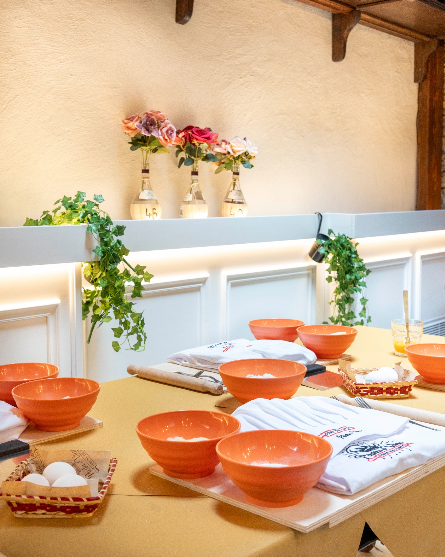 Cooking class table set with orange bowls, aprons, rolling pins, and fresh eggs